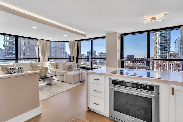 kitchen featuring white cabinets, open floor plan, a view of city, black electric cooktop, and stainless steel oven