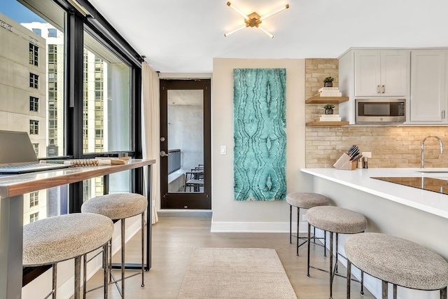 kitchen with tasteful backsplash, stainless steel microwave, light countertops, white cabinetry, and a sink