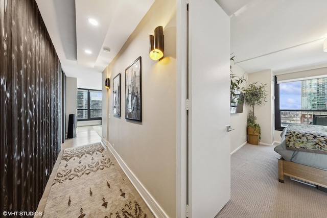 hall featuring a healthy amount of sunlight, light carpet, baseboards, and a city view