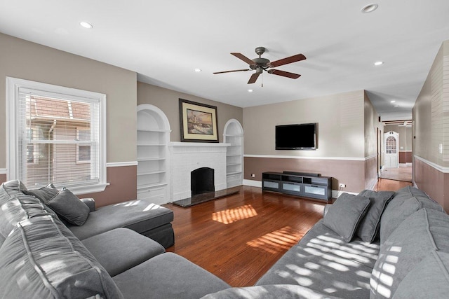 living room with hardwood / wood-style flooring, a fireplace, built in features, and ceiling fan