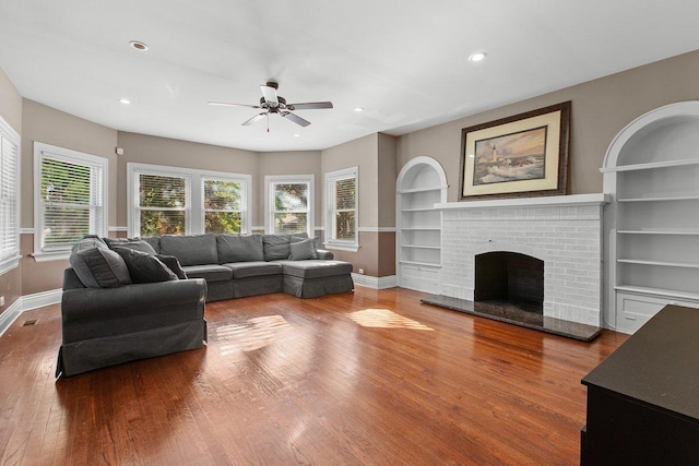 living room featuring a brick fireplace, built in shelves, and hardwood / wood-style floors