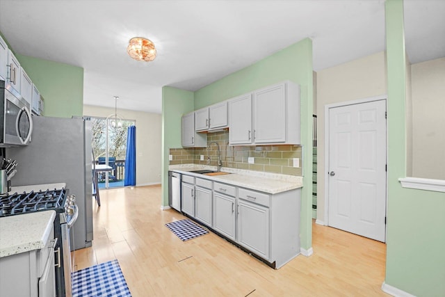 kitchen featuring sink, stainless steel appliances, tasteful backsplash, light hardwood / wood-style floors, and decorative light fixtures