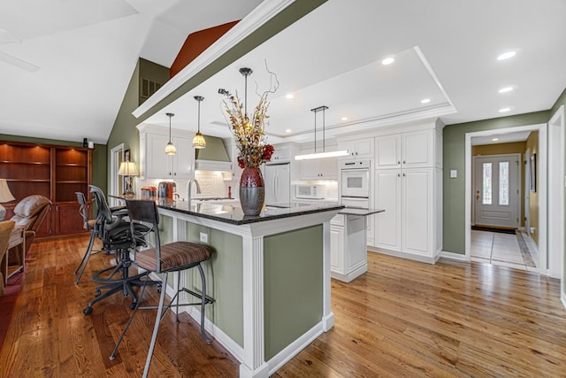 kitchen featuring decorative light fixtures, white appliances, a kitchen breakfast bar, and white cabinets