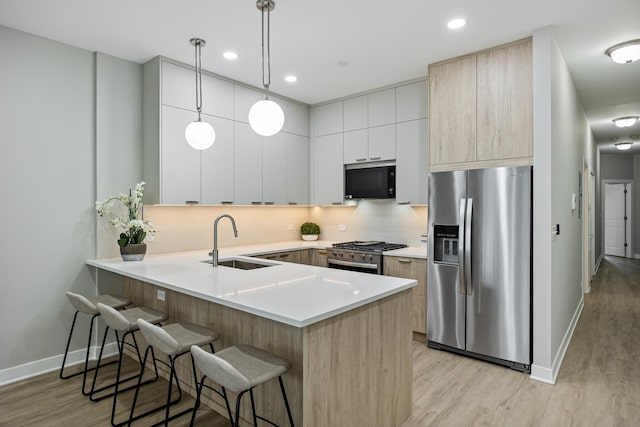 kitchen featuring sink, light hardwood / wood-style flooring, stainless steel appliances, decorative light fixtures, and kitchen peninsula