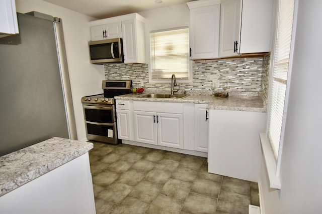 kitchen featuring appliances with stainless steel finishes, a wealth of natural light, white cabinetry, sink, and decorative backsplash