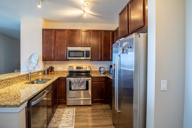 kitchen with sink, appliances with stainless steel finishes, light stone counters, light hardwood / wood-style floors, and kitchen peninsula