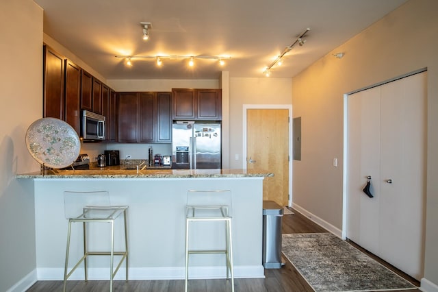 kitchen with light stone countertops, dark wood-type flooring, stainless steel appliances, and a kitchen bar