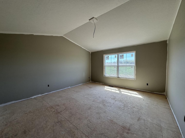 empty room featuring vaulted ceiling, a textured ceiling, and baseboards