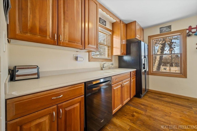 kitchen featuring dark wood-style floors, light countertops, brown cabinetry, a sink, and black appliances