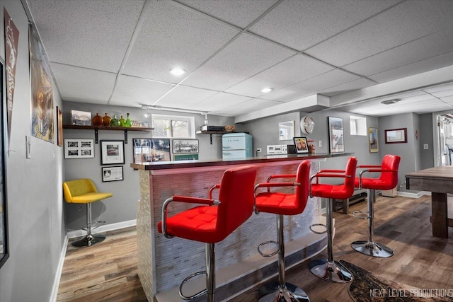 bar with a dry bar, a drop ceiling, and wood finished floors