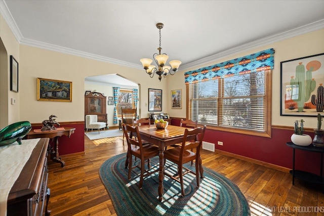 dining room featuring hardwood / wood-style flooring, crown molding, arched walkways, and a notable chandelier