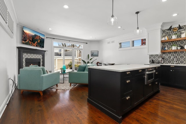 kitchen featuring decorative light fixtures, a tile fireplace, ornamental molding, dark wood-type flooring, and white cabinets