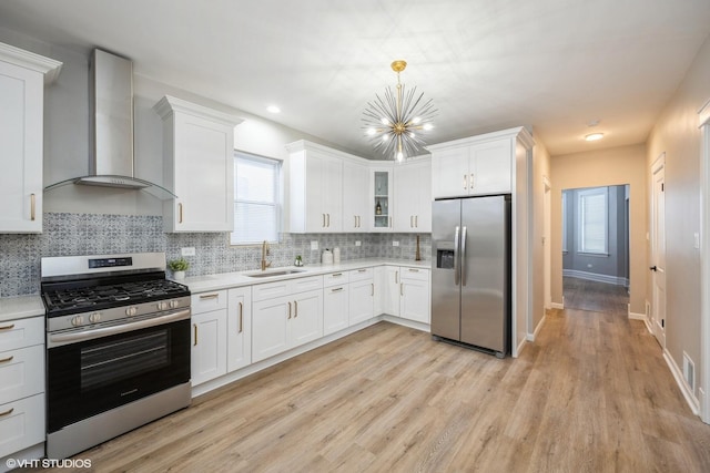 kitchen with light countertops, a notable chandelier, stainless steel appliances, wall chimney exhaust hood, and a sink