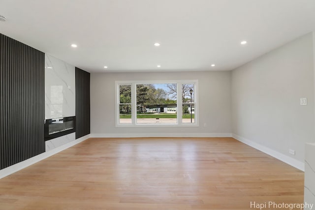 empty room with light wood-style floors, recessed lighting, baseboards, and a premium fireplace