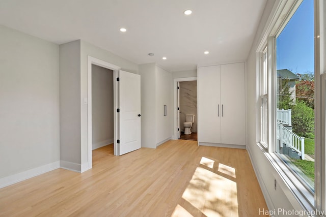 unfurnished bedroom featuring multiple windows, light wood-style flooring, recessed lighting, baseboards, and connected bathroom