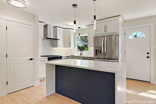 kitchen featuring stainless steel appliances, wall chimney range hood, light wood-type flooring, tasteful backsplash, and hanging light fixtures