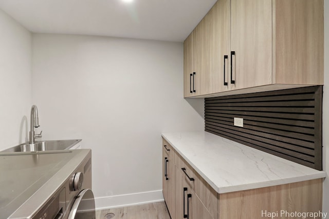 clothes washing area with light wood-type flooring, baseboards, and cabinet space