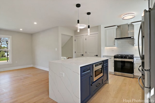 kitchen featuring appliances with stainless steel finishes, wall chimney exhaust hood, light wood-style flooring, backsplash, and a kitchen island