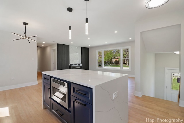 kitchen featuring stainless steel microwave, light wood-type flooring, pendant lighting, light stone countertops, and open floor plan