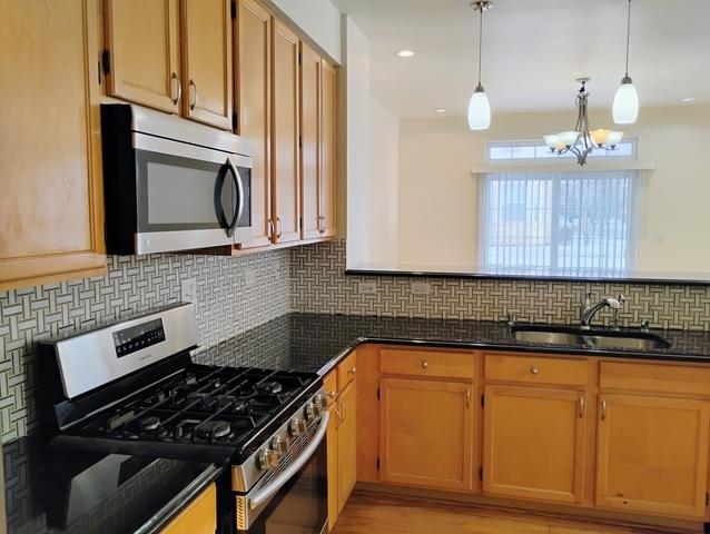 kitchen with pendant lighting, sink, appliances with stainless steel finishes, dark stone countertops, and backsplash