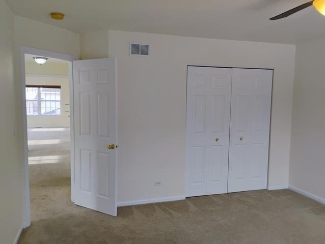 unfurnished bedroom with light colored carpet, ceiling fan, and a closet