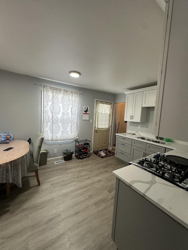 kitchen featuring gray cabinets, white cabinetry, sink, light stone counters, and light hardwood / wood-style flooring