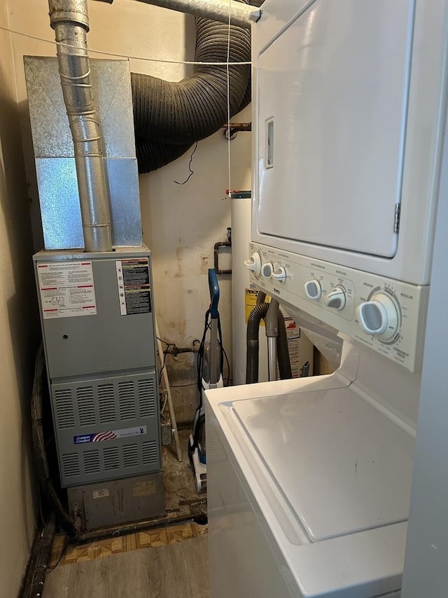 laundry room featuring stacked washer and clothes dryer, heating unit, and hardwood / wood-style floors