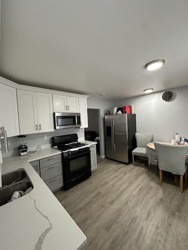 kitchen featuring sink, light hardwood / wood-style flooring, white cabinetry, stainless steel appliances, and light stone countertops