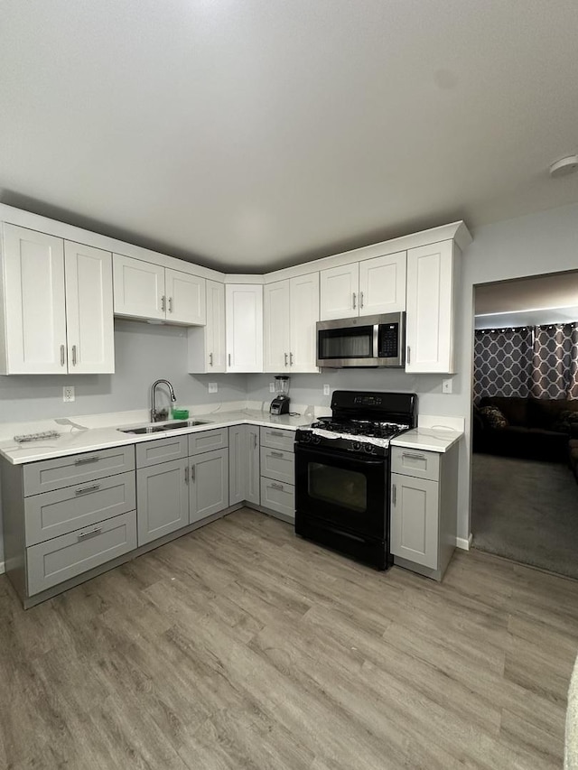 kitchen with sink, gray cabinetry, white cabinetry, light hardwood / wood-style flooring, and black gas range