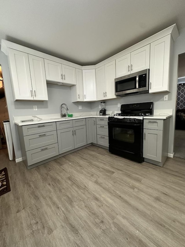 kitchen featuring sink, gray cabinetry, white cabinets, gas stove, and light hardwood / wood-style flooring