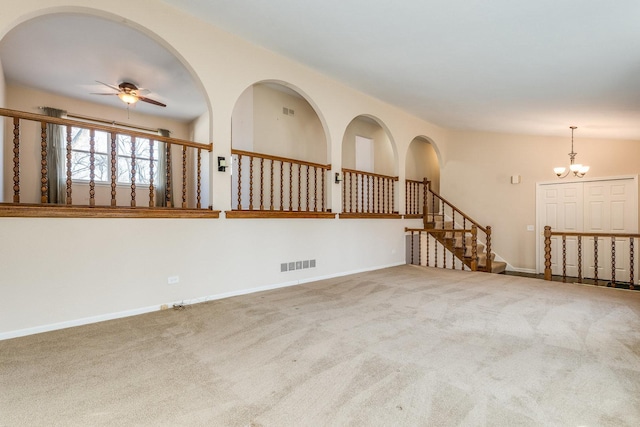 carpeted spare room featuring stairs, ceiling fan with notable chandelier, visible vents, and baseboards