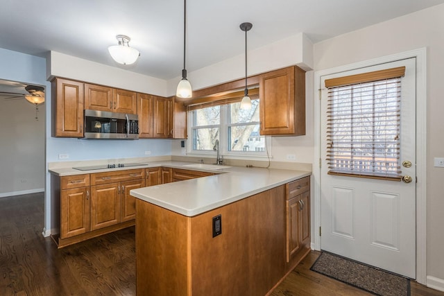 kitchen with stainless steel microwave, brown cabinets, a peninsula, black electric cooktop, and a sink