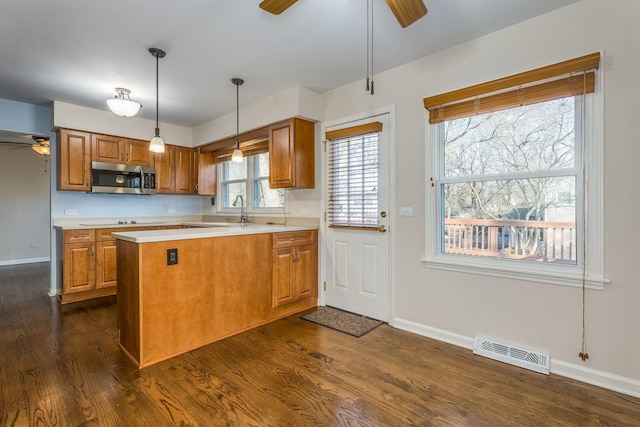 kitchen with stainless steel microwave, brown cabinets, visible vents, and ceiling fan