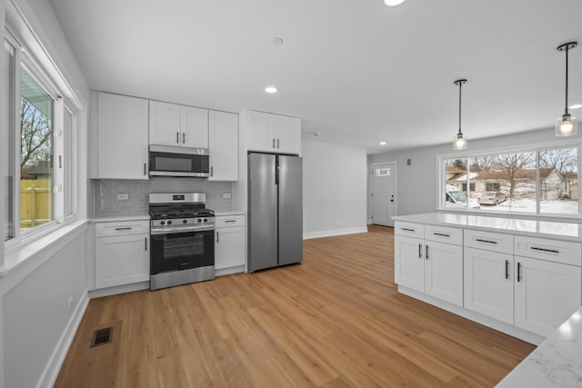 kitchen with white cabinetry, stainless steel appliances, decorative light fixtures, and backsplash