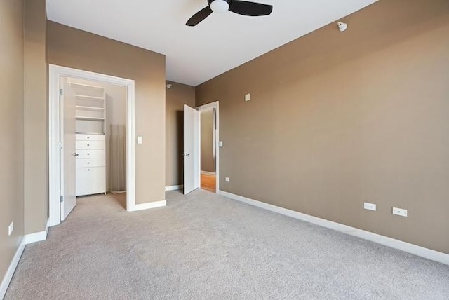 unfurnished bedroom with a walk in closet, light colored carpet, a closet, and ceiling fan