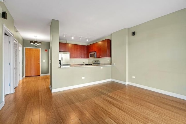 kitchen featuring appliances with stainless steel finishes, decorative light fixtures, a notable chandelier, light hardwood / wood-style floors, and kitchen peninsula