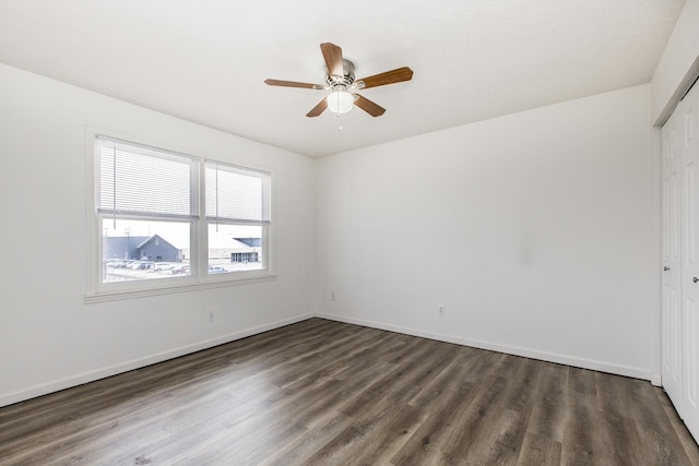 empty room featuring a ceiling fan, dark wood-style flooring, and baseboards