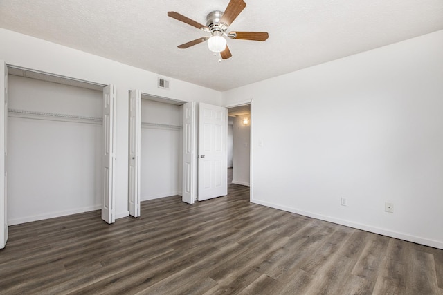 unfurnished bedroom with a textured ceiling, wood finished floors, visible vents, baseboards, and multiple closets