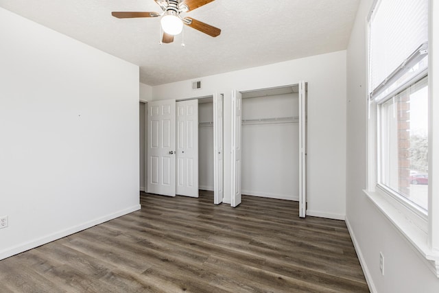 unfurnished bedroom featuring a textured ceiling, baseboards, dark wood finished floors, and multiple closets