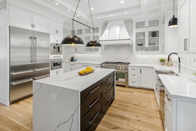 kitchen with premium range hood, decorative light fixtures, sink, high end appliances, and a center island