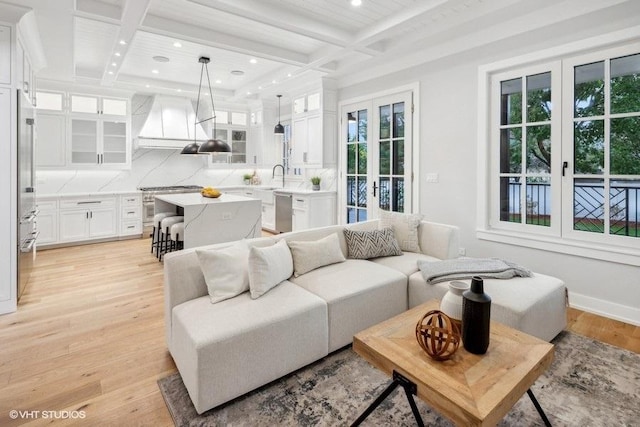 living room with sink, beam ceiling, coffered ceiling, light hardwood / wood-style floors, and french doors