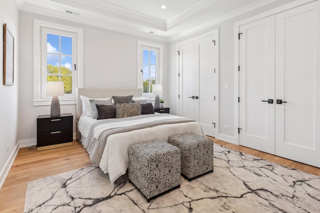 bedroom with ornamental molding, hardwood / wood-style floors, multiple windows, and two closets