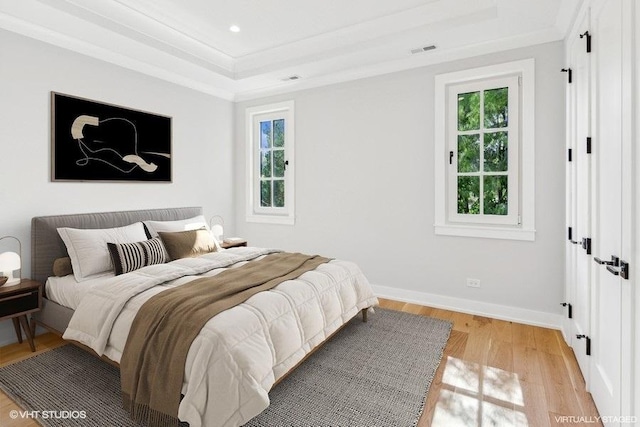 bedroom with ornamental molding, a raised ceiling, multiple windows, and light wood-type flooring