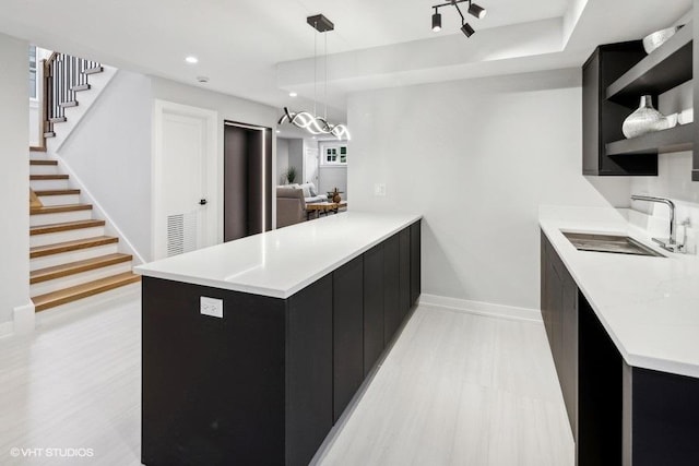 kitchen with hanging light fixtures, sink, light wood-type flooring, and kitchen peninsula