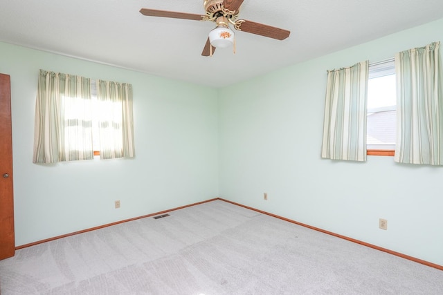 empty room featuring ceiling fan, light colored carpet, and a wealth of natural light