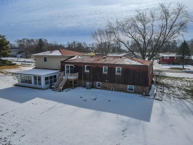 snow covered back of property with a sunroom