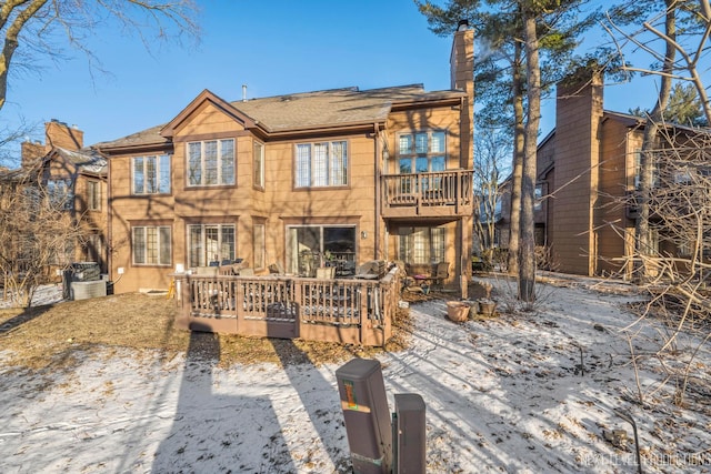 snow covered house featuring a wooden deck and a balcony