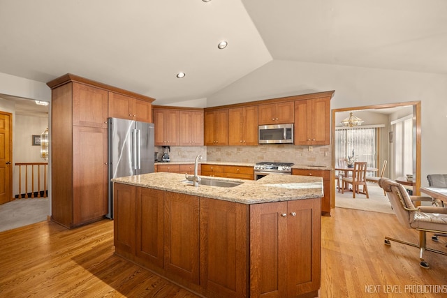 kitchen featuring sink, stainless steel appliances, light stone counters, an island with sink, and vaulted ceiling