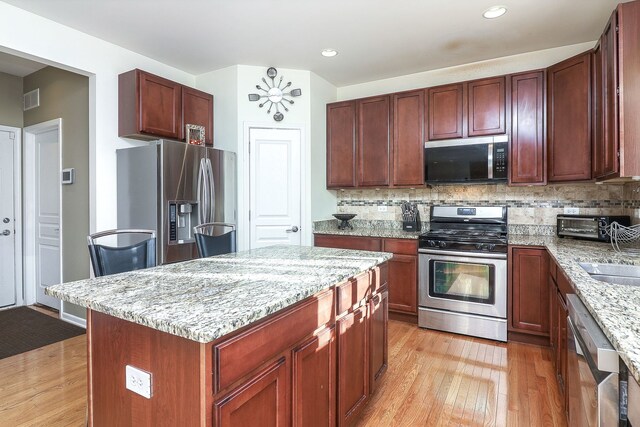 kitchen featuring appliances with stainless steel finishes, backsplash, light stone counters, light hardwood / wood-style floors, and a kitchen island