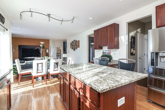 kitchen with light stone countertops, a center island, stainless steel fridge, and light wood-type flooring